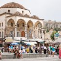 Athenians and tourists in Monastiraki Square in Athens, Greece, with market stalls, Tzistarakis Mosque and the Acropolis in the background.